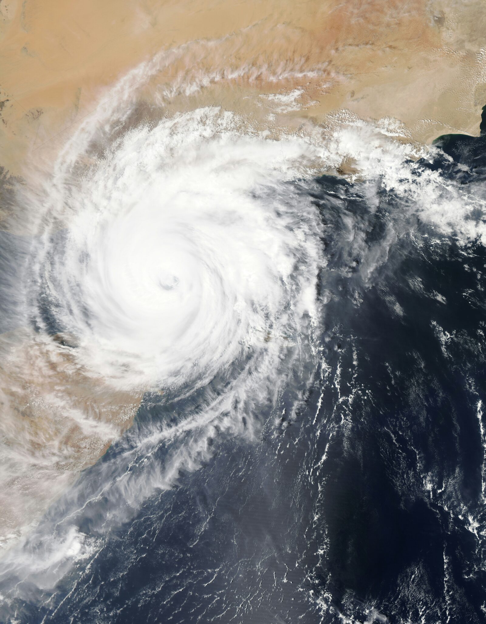 Satellite view of a large, spiraling cyclone over a landmass and ocean, showing dense white clouds and swirling patterns.