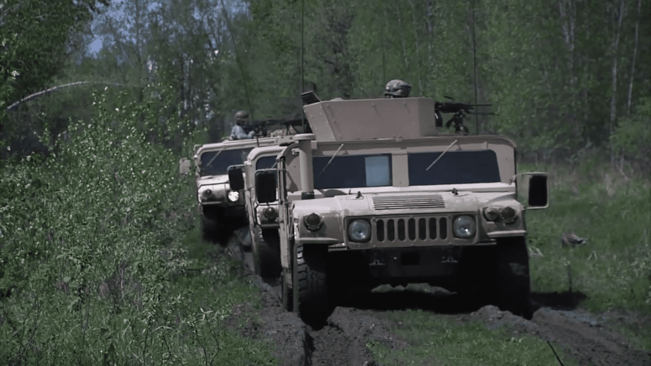 Military vehicles driving through a forested dirt path.