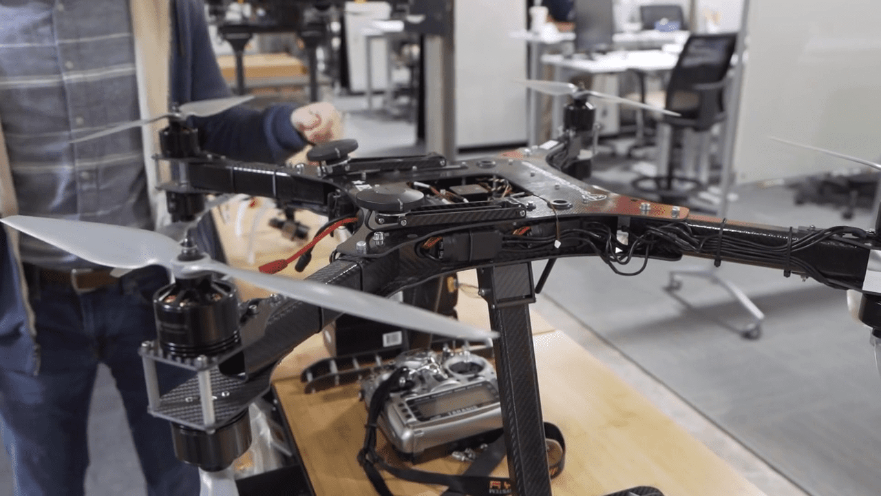 A technician adjusts a large drone on a workbench. There are tools and equipment in the background.