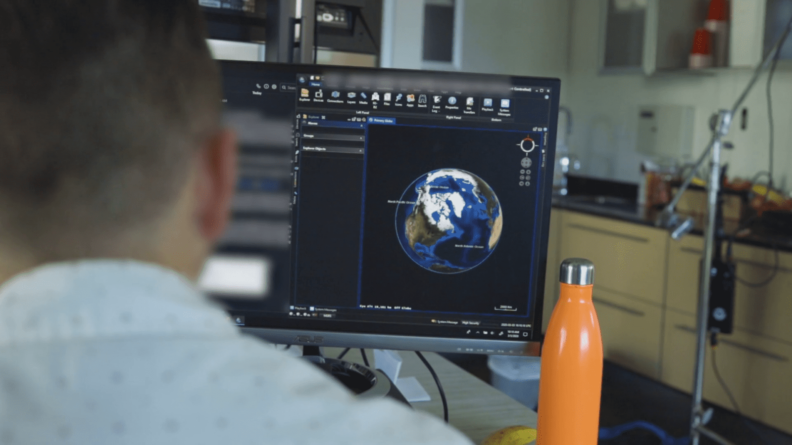 Person viewing a computer screen displaying a digital globe. An orange water bottle is on the desk.