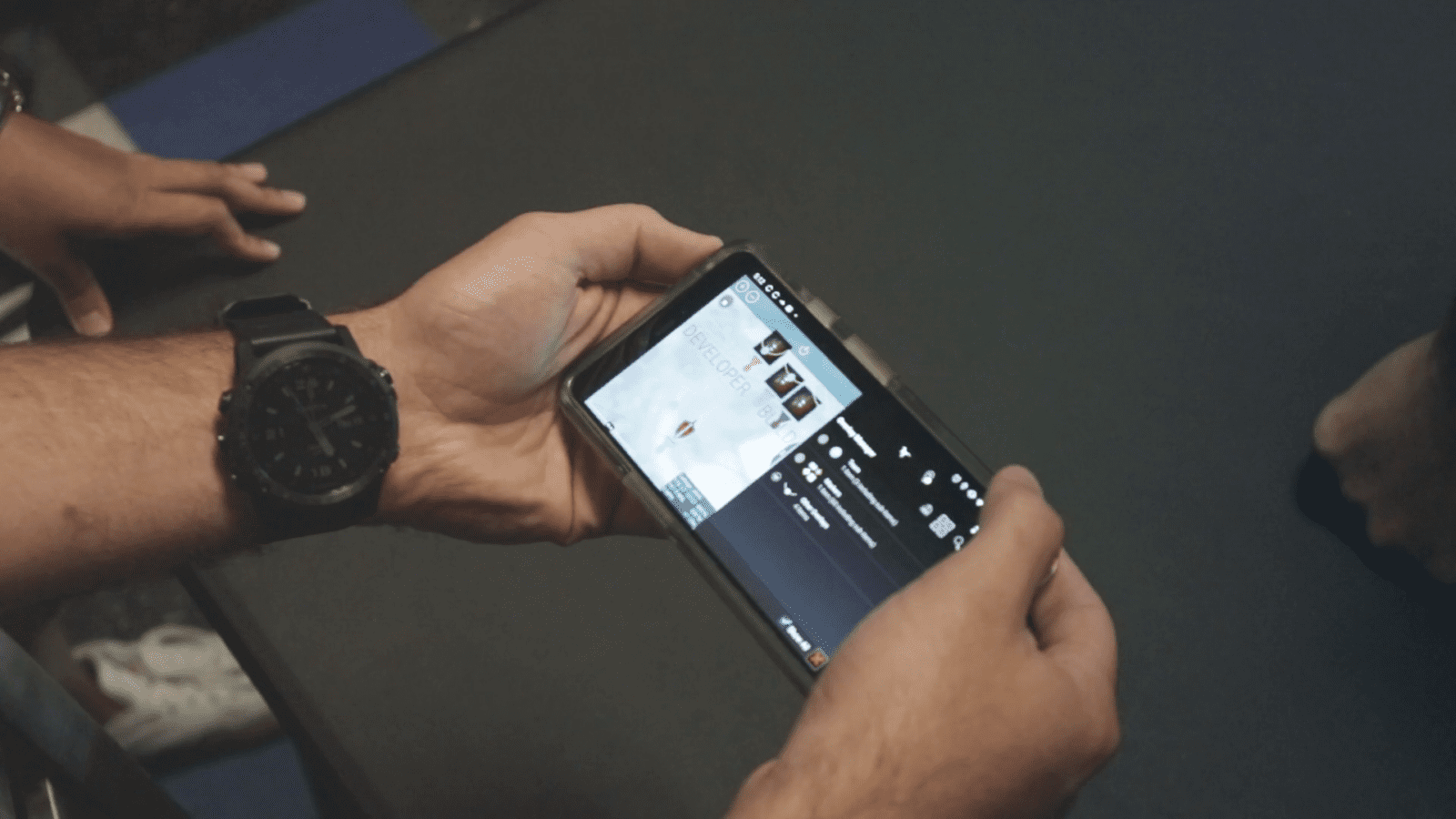 Person holding a smartphone horizontally, watching a video on YouTube. The screen displays video details and a portion of the playback interface.