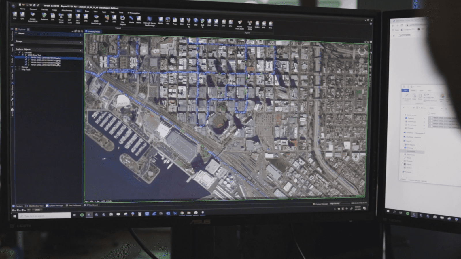 Computer screen displaying an aerial map of a coastal city area with marked routes and surrounding buildings.