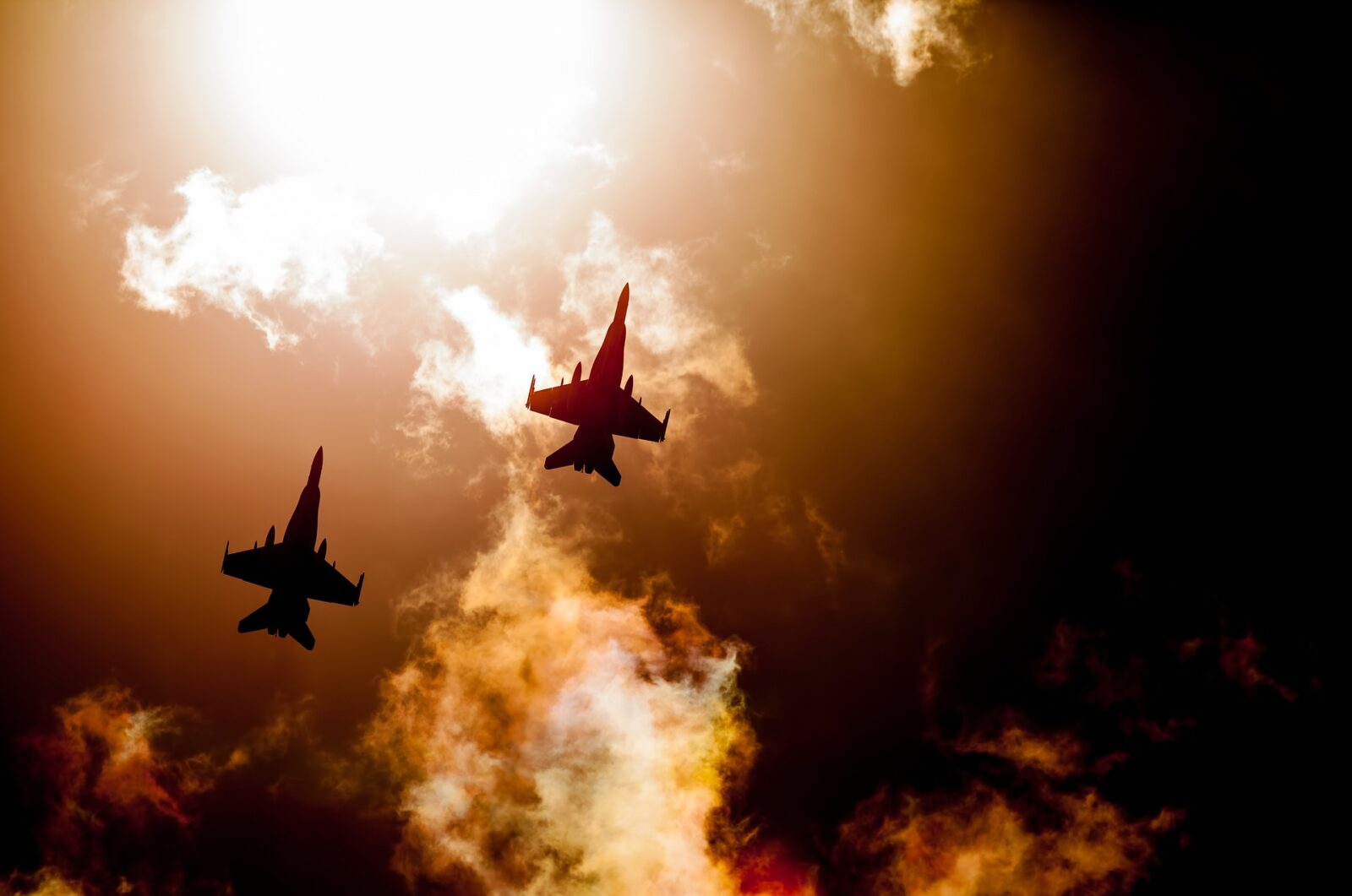 Two fighter jets silhouetted against a dramatic sunset sky with clouds.