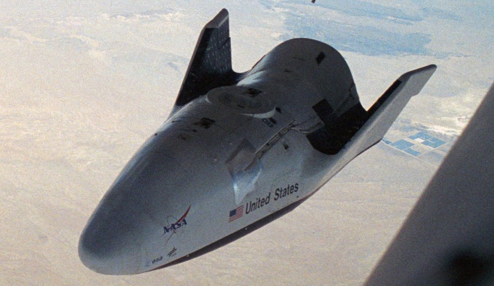 A spaceplane with NASA and United States logos is flying over a desert landscape.