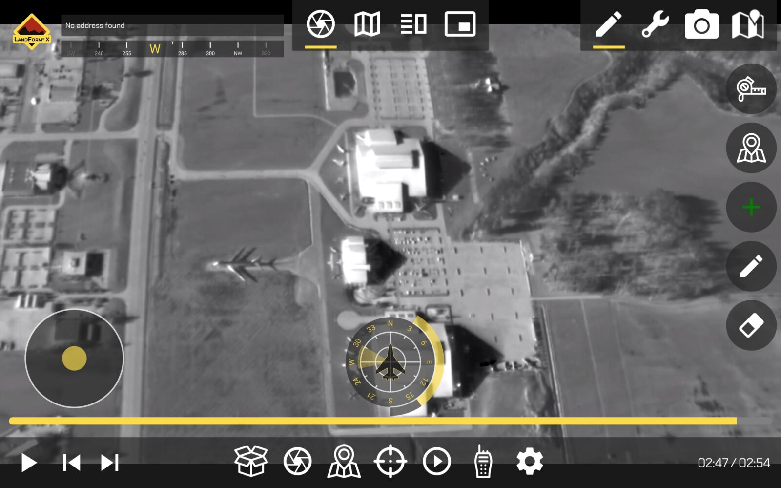 Aerial infrared view of a complex with three main buildings, roads, and a parked airplane. Navigation interface overlays with compass and controls spotted on screen.