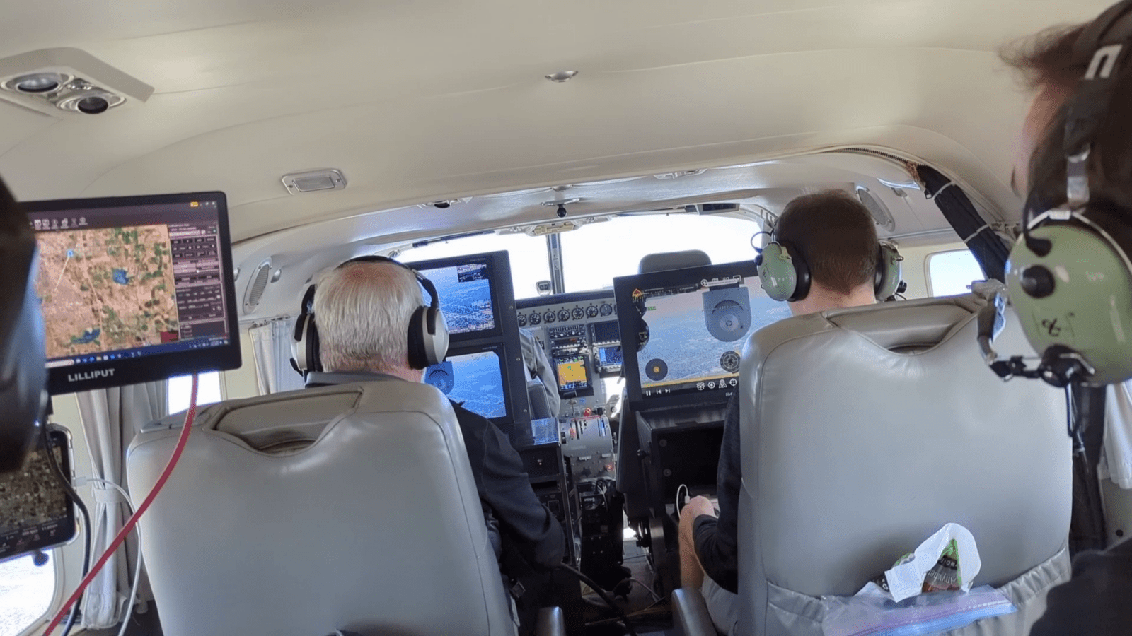 Two pilots in a cockpit with headsets, monitoring flight instruments and screens.
