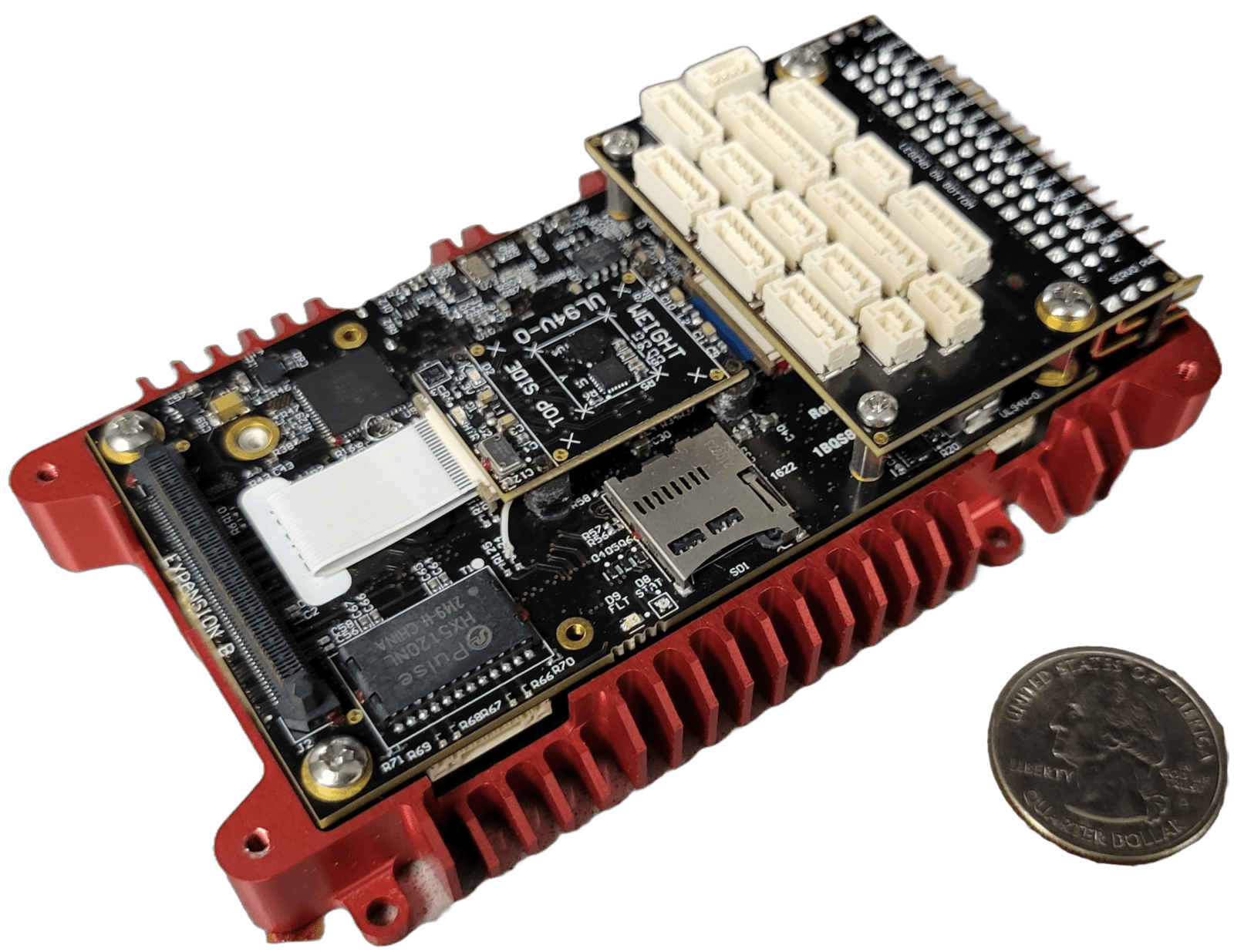 A small electronic circuit board with various connectors and components is shown next to a U.S. quarter for scale. The board has a red heat sink and a microSD card slot.