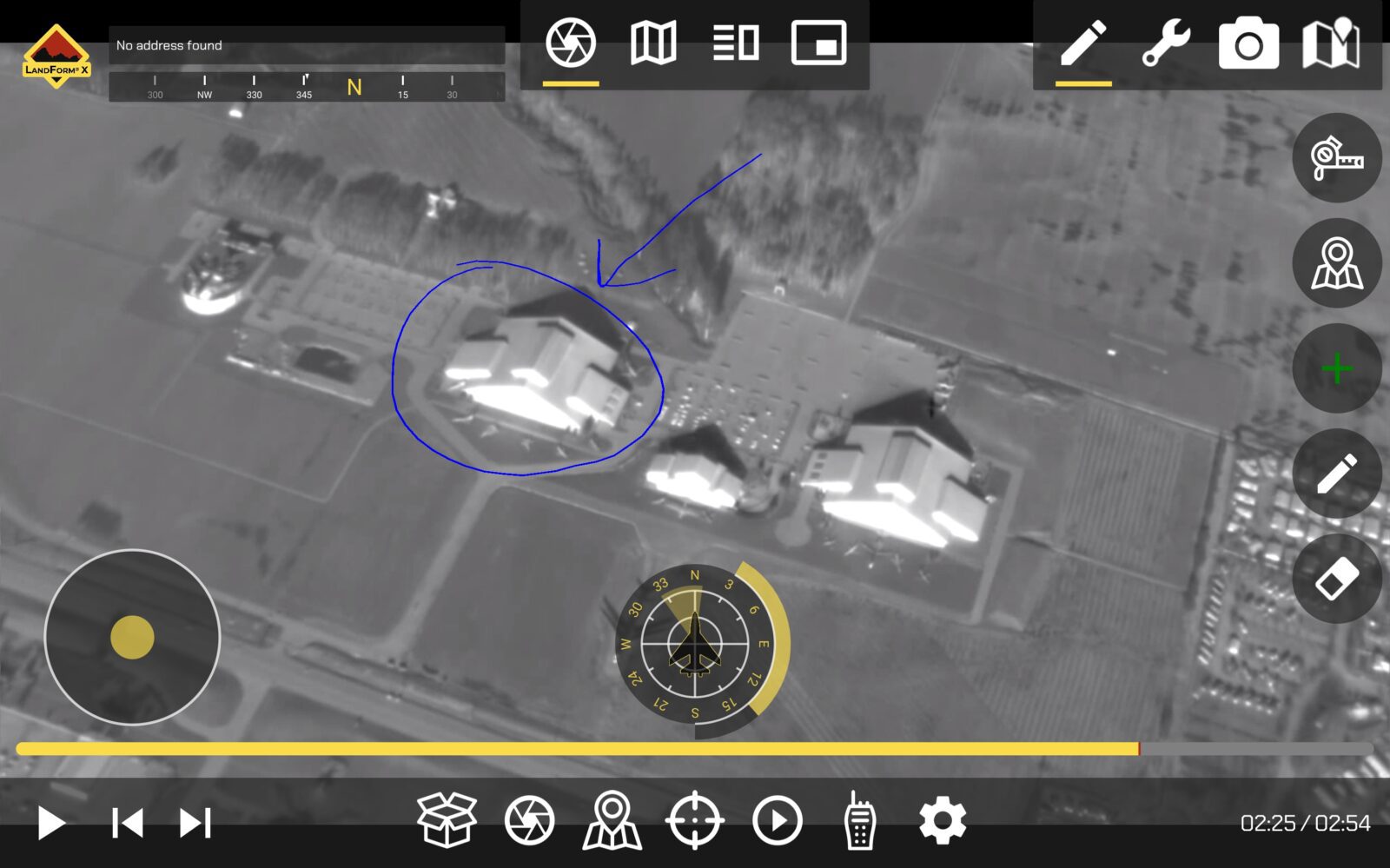 Aerial thermal image showing three large buildings with a blue arrow pointing to one. There are fields surrounding the buildings. Several digital icons and a compass overlay the image.